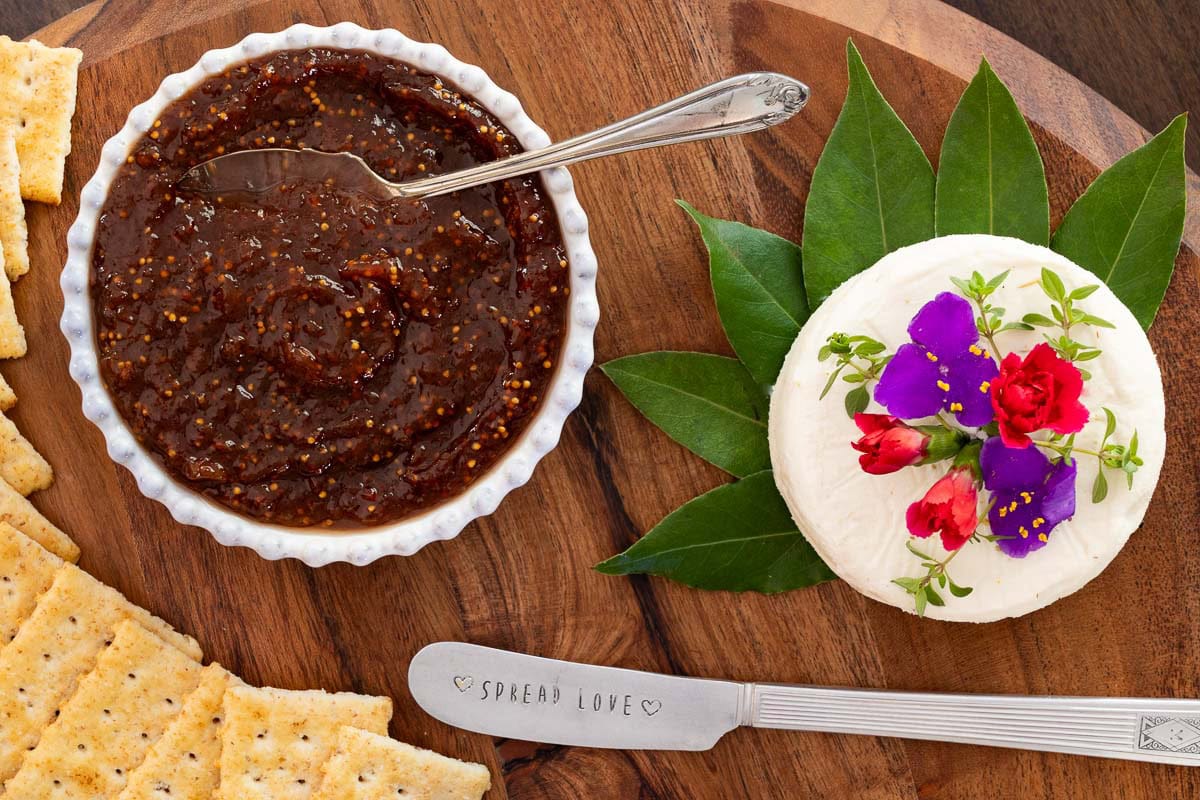 Close-up of of a charcuterie board with a small bowl of strawberry balsamic fig jam, and a round of goat cheese with tiny edible flowers on top.