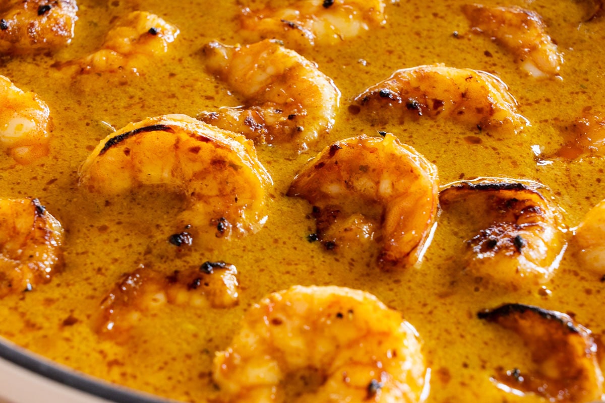 Close-up of broiled shrimp in a creamy Thai coconut curry sauce, highlighting the golden char and velvety texture of the vibrant yellow curry.