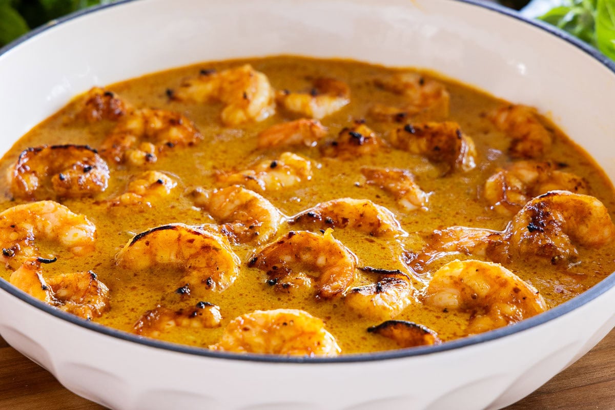 Broiled shrimp in a creamy Thai coconut curry sauce, served in a white braiser pan with a golden, lightly charred finish.