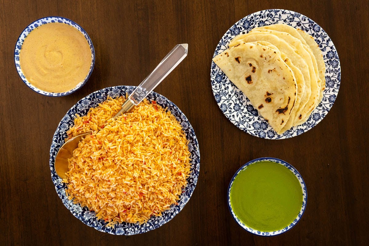 Overhead photo of a bowl of Easy Mexican Rice, Homemade Flour Tortillas, and dishes of Mexican Cilantro Sauce and Creamy Chipotle Sauce