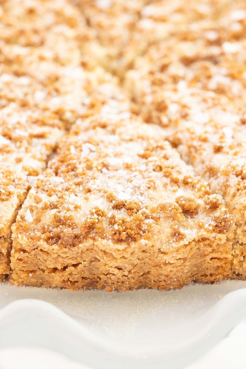 Close-up of a wedge of Biscoff shortbread showing a golden, crumbly texture with a crisp Biscoff topping and flaky sea salt