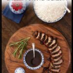 Sliced grilled pork tenderloin with balsamic fig glaze on a wooden board, served with a bowl of glaze, a sprig of rosemary, and a side of white rice in a blue and white bowl.