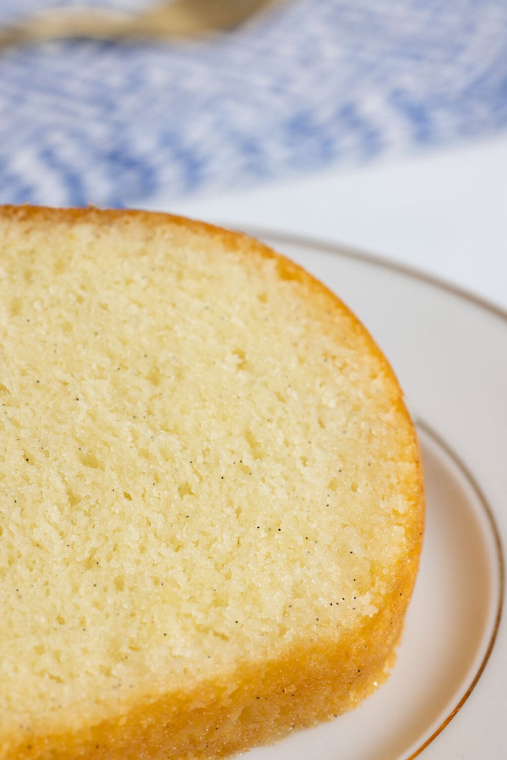 close up of the vanilla bean bundt cake with vanilla bean specks visible on a plate with a blue and white background
