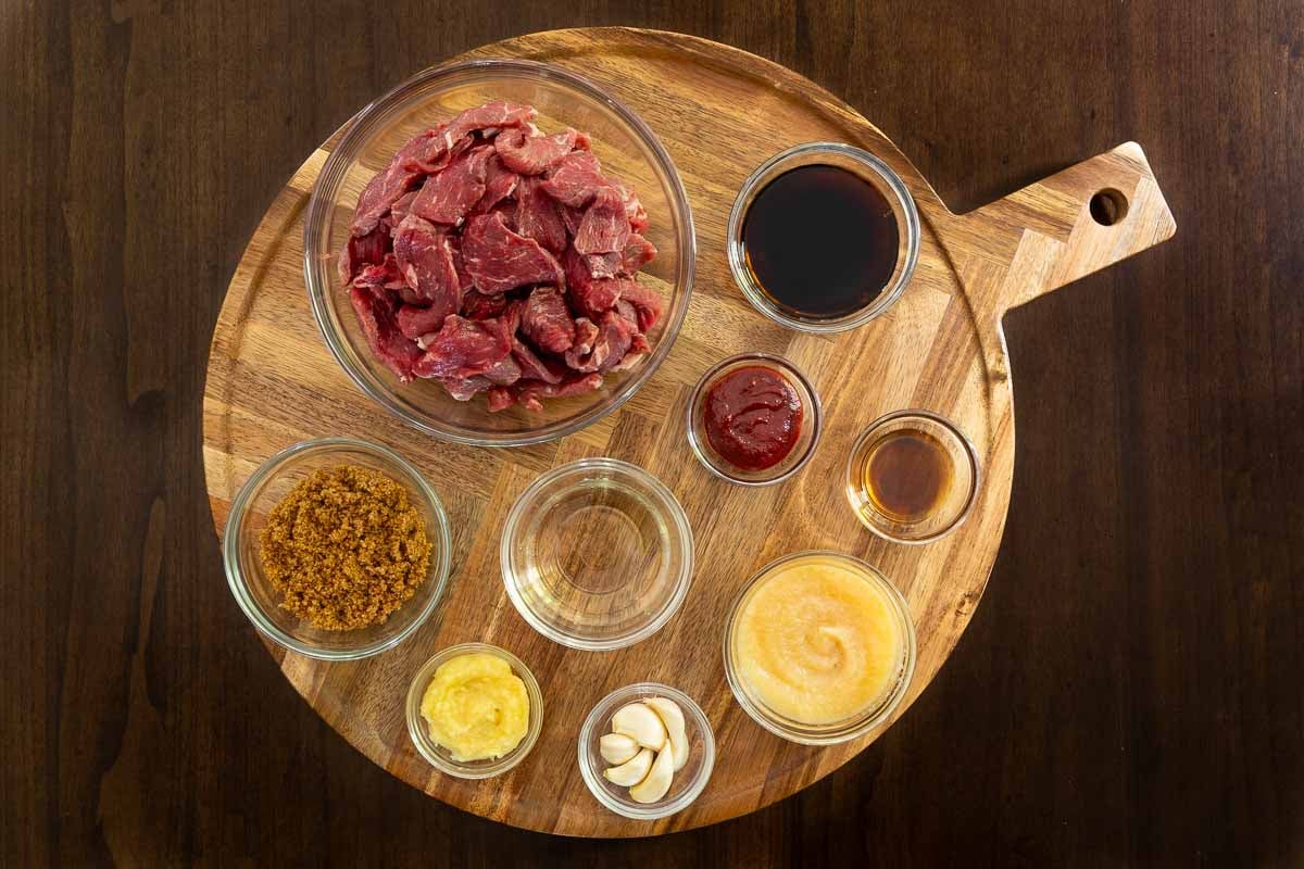 Ingredients for Korean beef skewers including sliced steak, soy sauce, gochujang, brown sugar, ginger, garlic, rice vinegar, sesame oil, and applesauce.