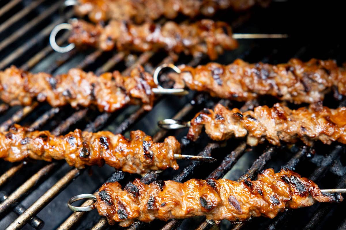 Grilled Korean beef skewers cooking over high heat, caramelized and slightly charred on the grill grates