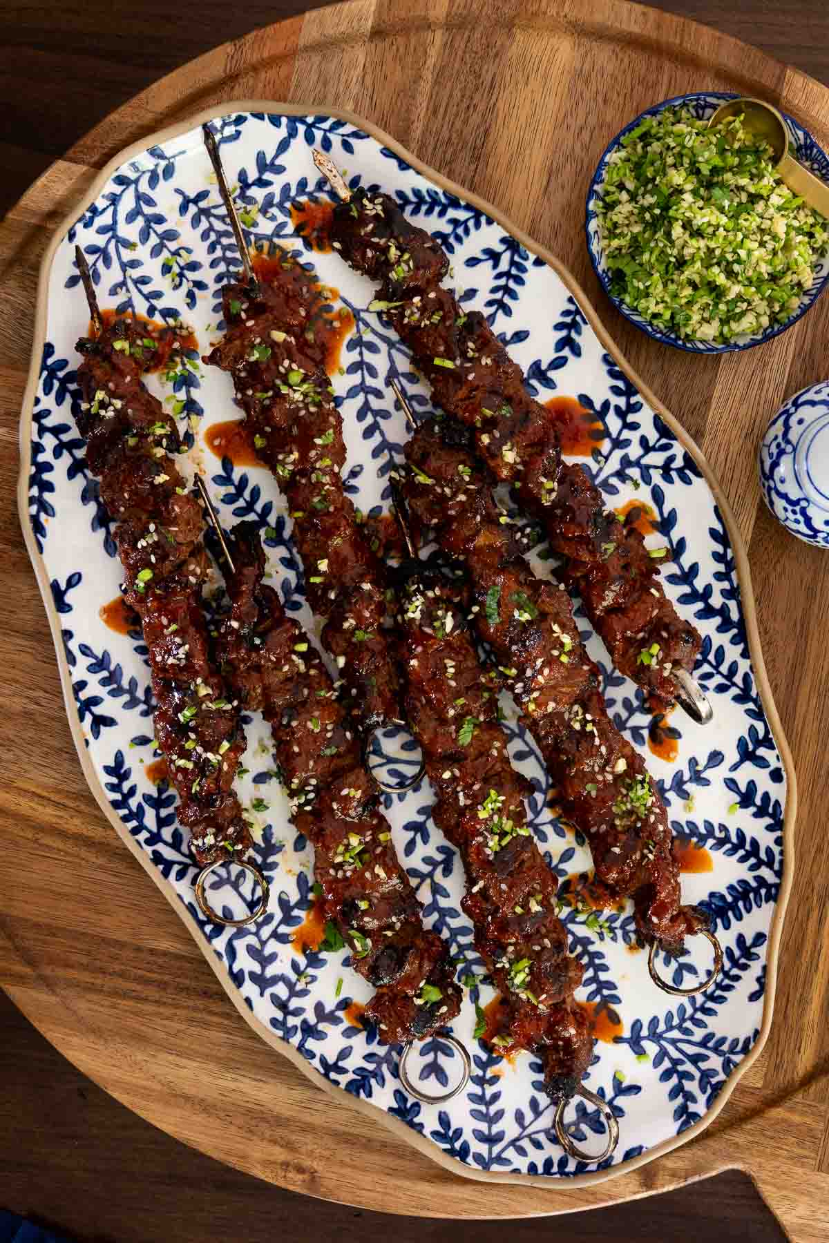 Grilled Korean beef skewers served on a patterned platter with scallion-cilantro gremolata.