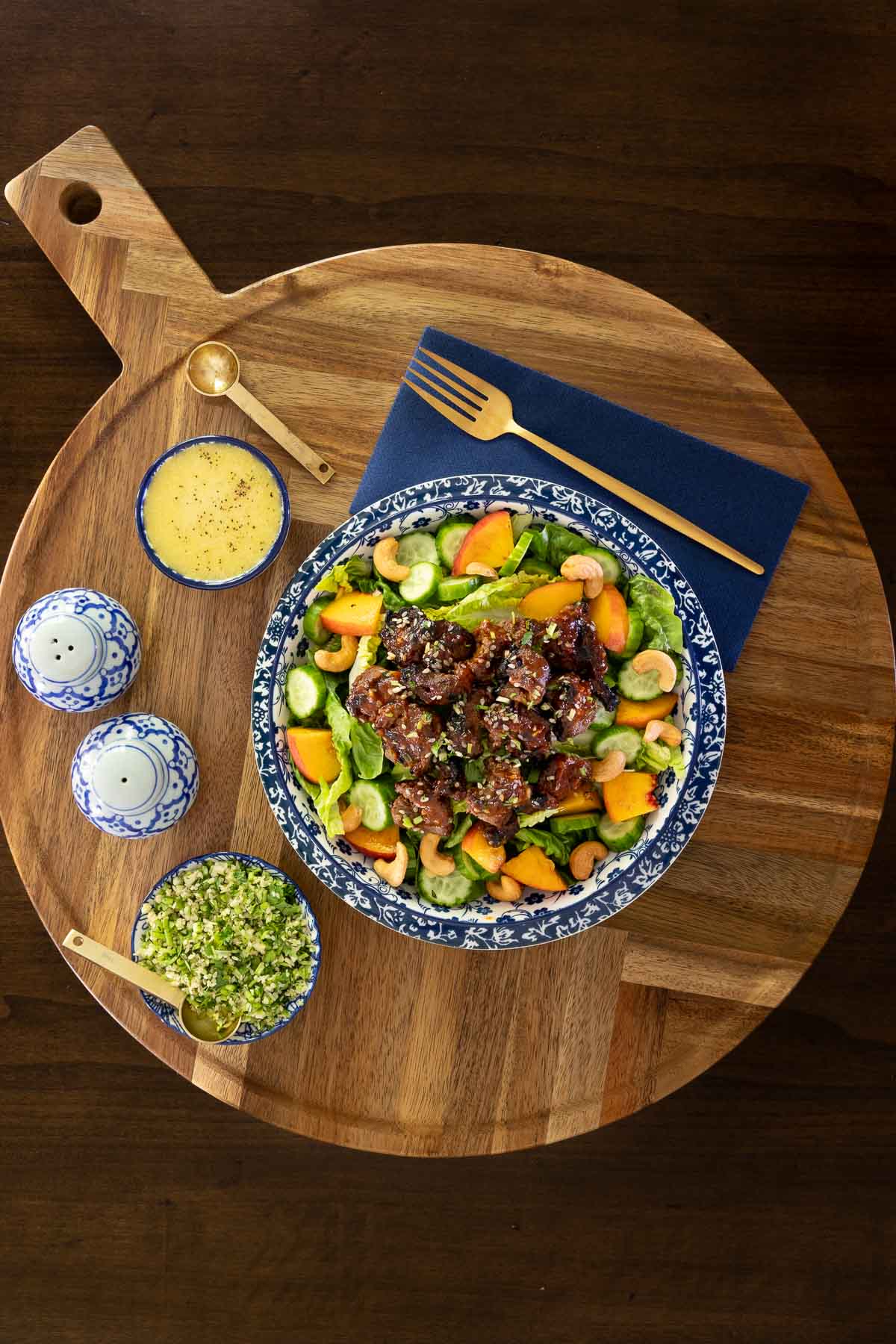 Grilled Korean beef skewers served in a vibrant salad with romaine, cucumbers, peaches, cashews, and sesame seeds, with dressing and gremolata on the side.