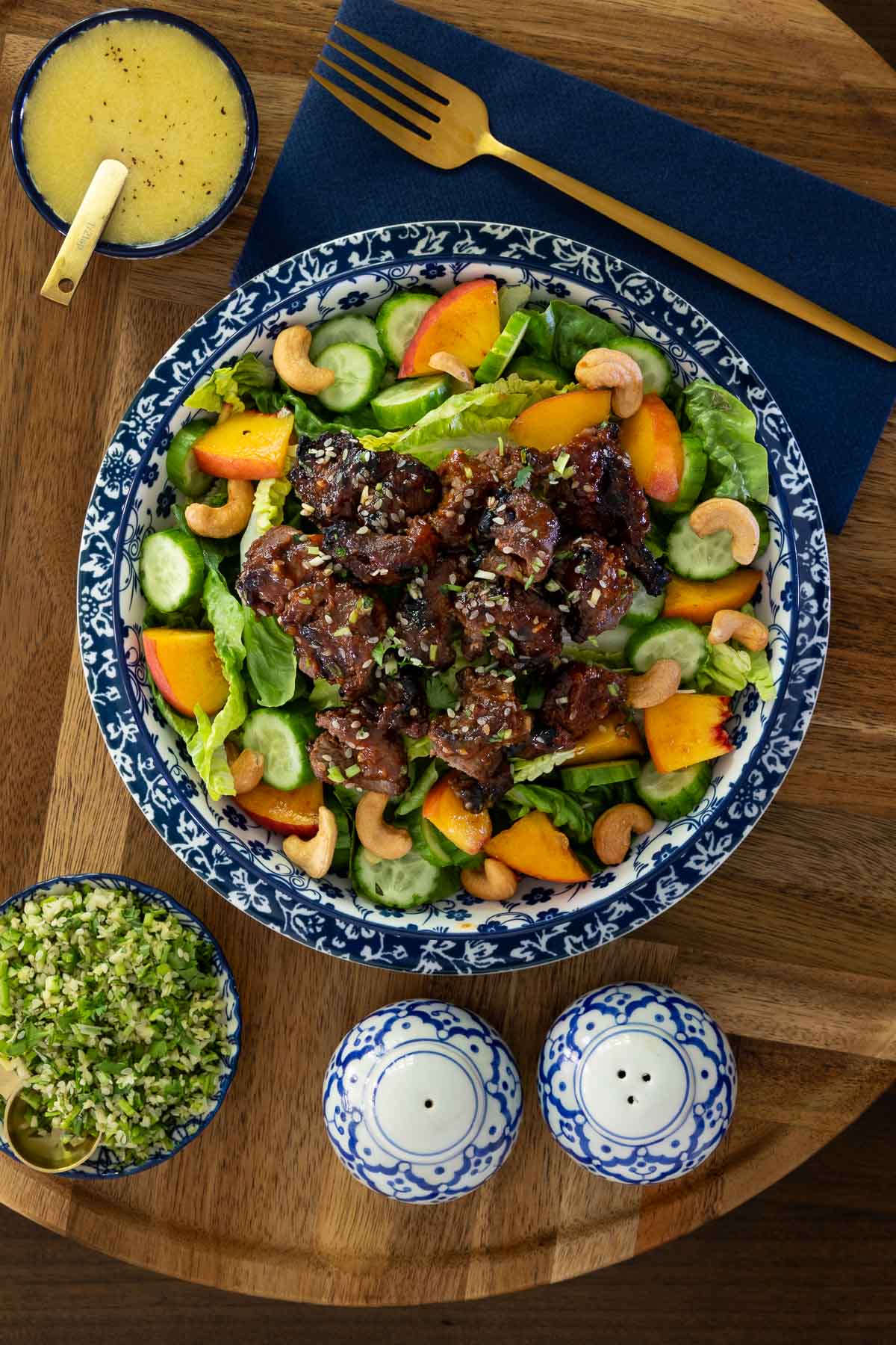 Grilled Korean beef skewers served in a vibrant salad with romaine, cucumbers, peaches, cashews, and sesame seeds, with dressing and gremolata on the side.