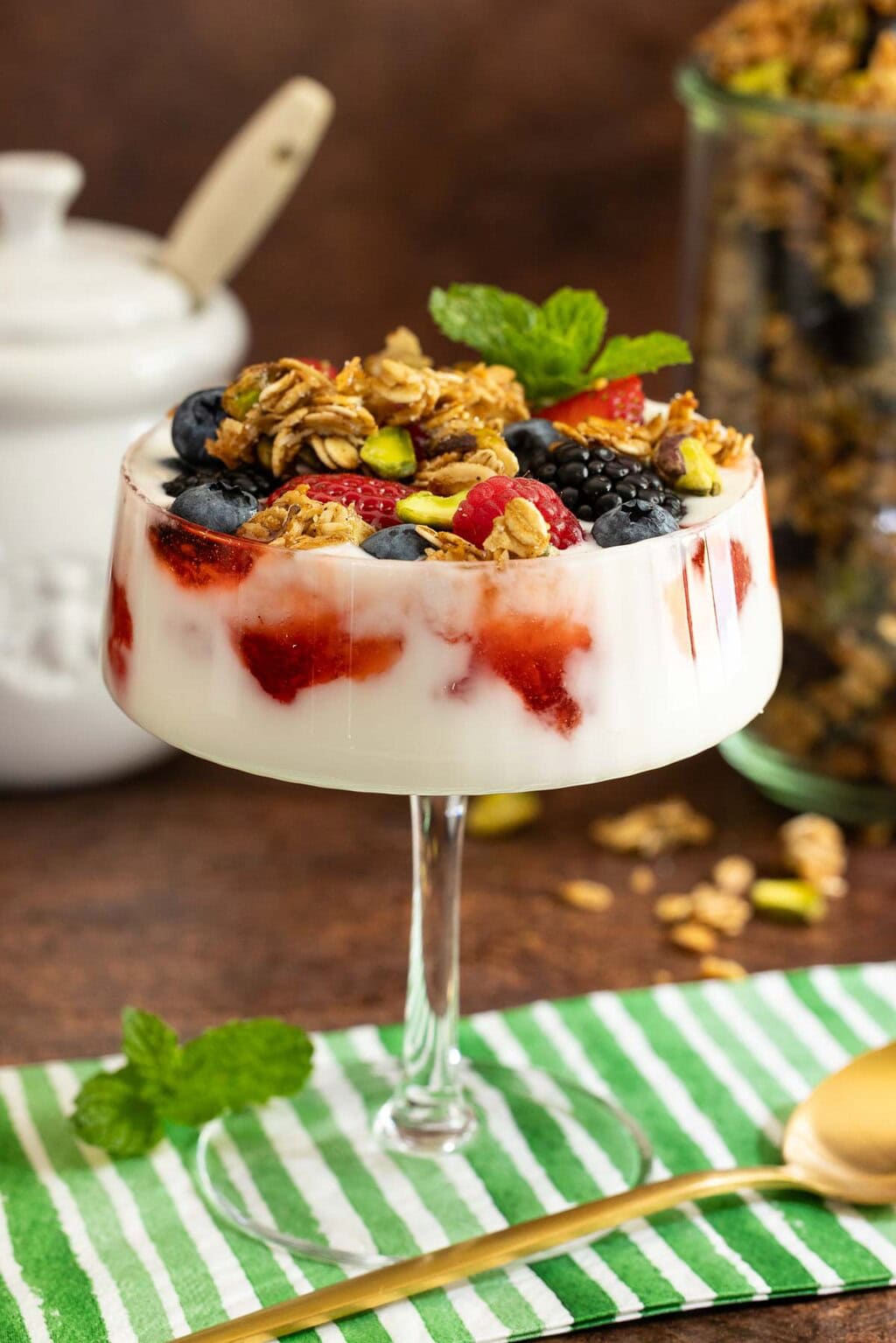 Yogurt parfait layered with fresh strawberries, blackberries, blueberries, and crunchy Maple Pistachio Granola, garnished with mint and served in a glass.