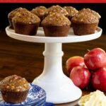 Honey apple bran muffins on a white cake stand with apples stacked in the background and a small dish of butter.