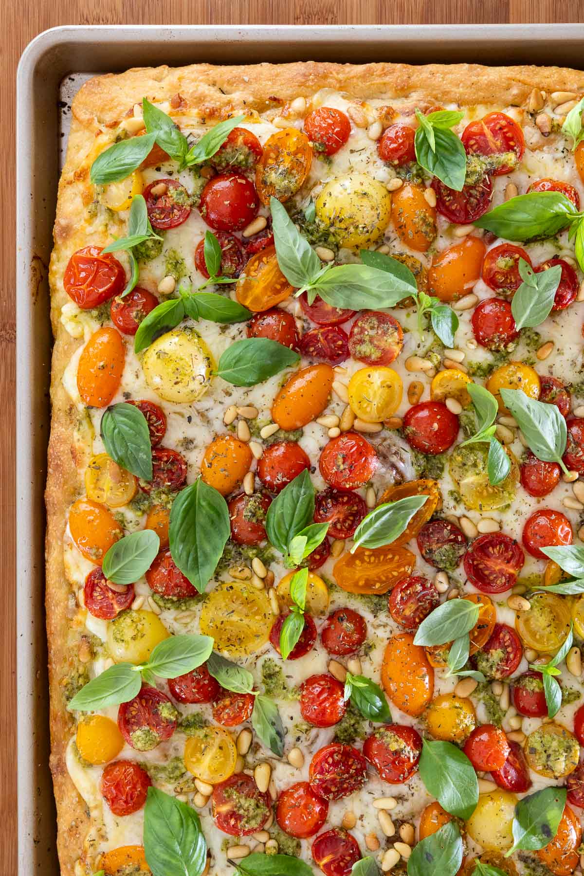 Overhead view of Easy Sheet Pan Pizza Margherita with golden focaccia crust, melted mozzarella, salted cherry tomatoes, pesto drizzle, pine nuts, and fresh basil leaves