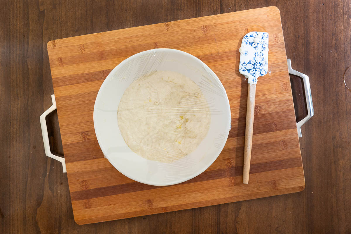 Focaccia-style dough for Easy Sheet Pan Pizza Margherita resting in a bowl covered with plastic wrap to rise