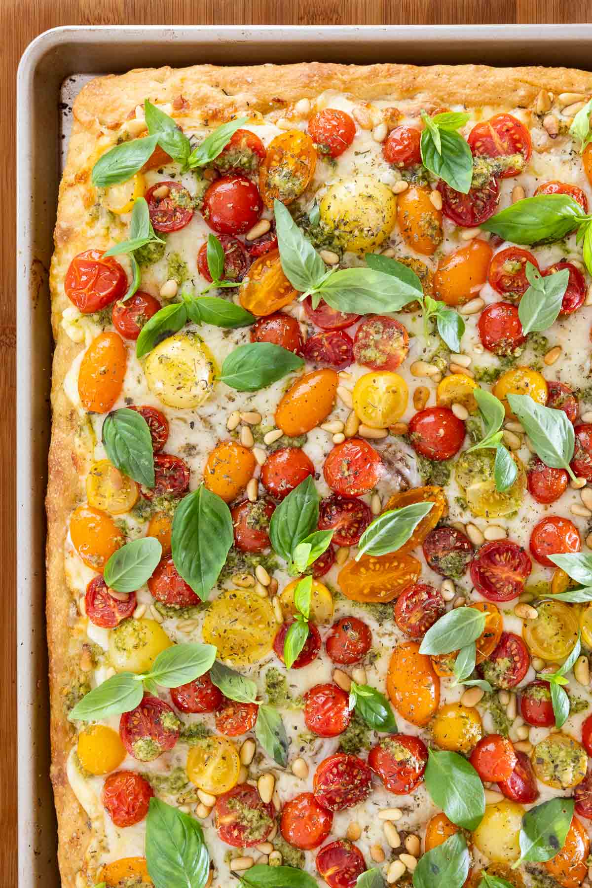 close up of finished magherita pizza with fresh tomatoes, basil, pine nuts, dried hers and a golden crust in a sheet pan