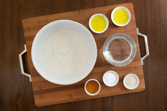 Ingredients for Easy Sheet Pan Pizza Margherita focaccia crust- flour, water, olive oil, honey, salt, and yeast on a wooden board