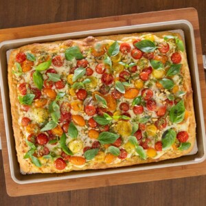 Easy Sheet Pan Pizza Margherita with focaccia crust, mozzarella, cherry tomatoes, pesto drizzle, and fresh basil in a baking pan.
