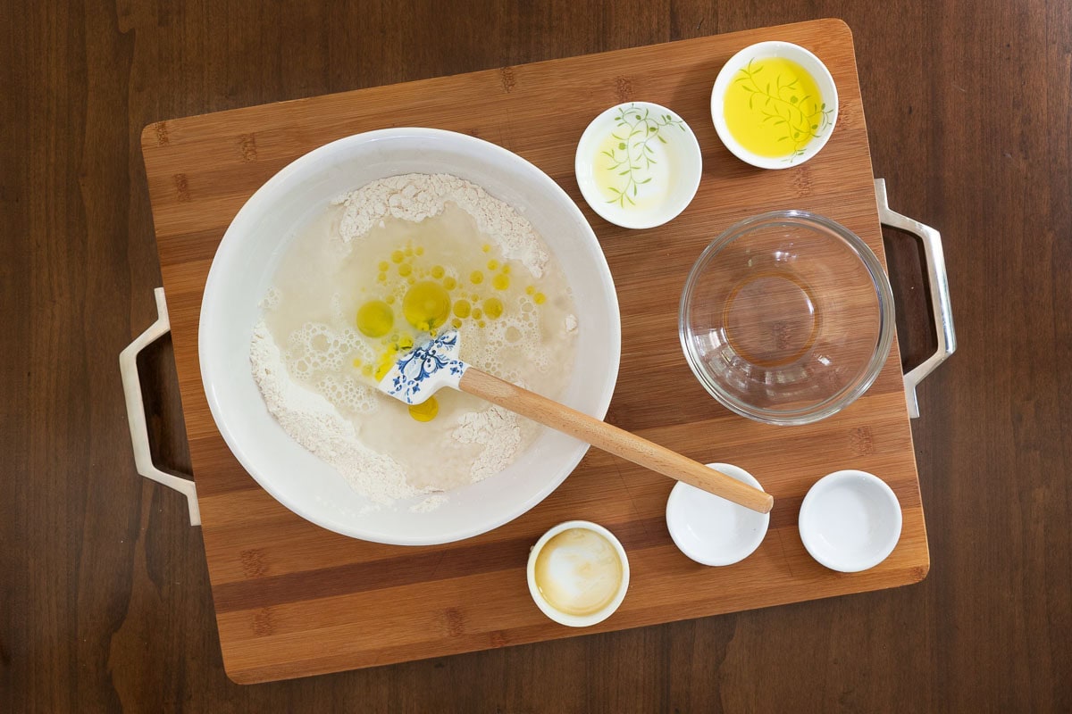 Mixing focaccia-style dough for Easy Sheet Pan Pizza Margherita -flour, water, olive oil, and yeast in a white bowl with a spatula