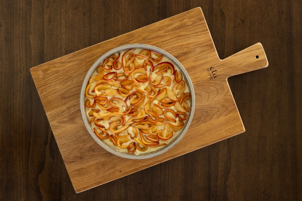 Overhead view of unbaked Italian Apple Ricotta Cake in a round pan, with thin cinnamon apple slices arranged over ricotta batter.