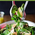 Apple and spinach salad in a pewter bowl with salad tongs.