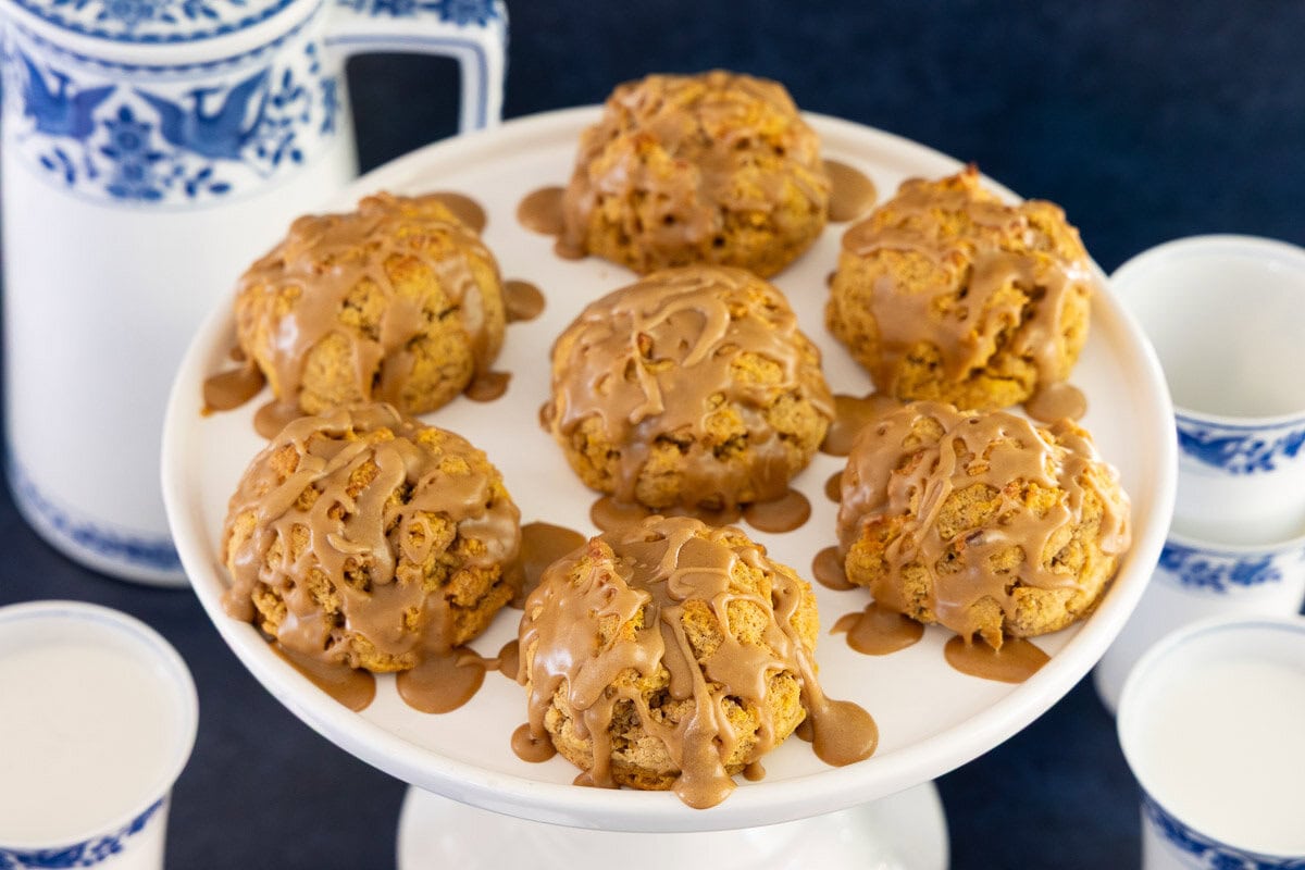 Pedestal serving plate of golden pumpkin scones topped with salted caramel glaze, a cozy and easy fall baking recipe.