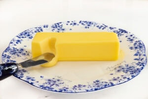 Stick of very soft salted butter on a blue and white floral plate with a butter knife.