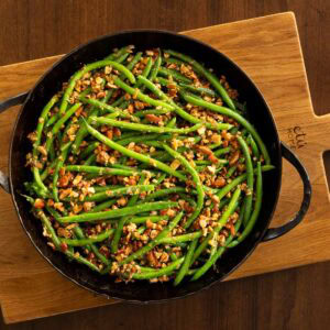 Brown Butter Green Beans Almondine in a boack skillet on a wooden cutting board.