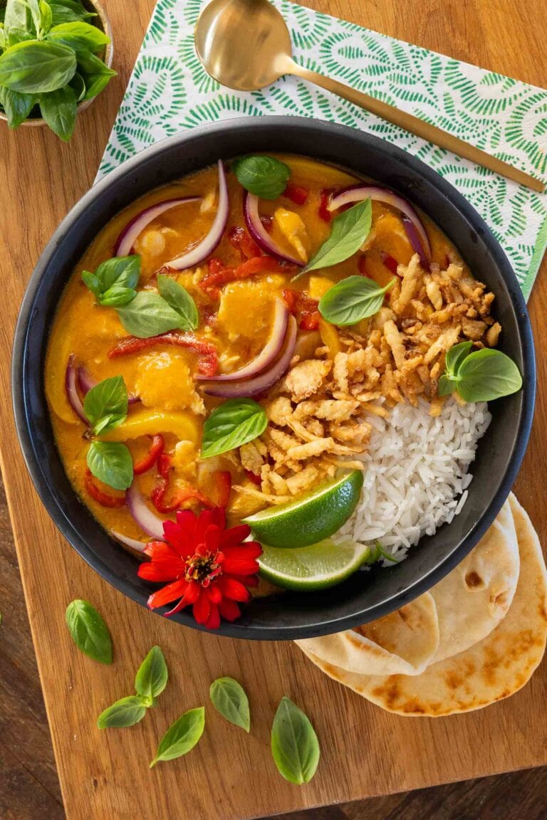 Lemongrass coconut chicken curry in a black bowl with rice and limes.