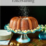 Apple cider bundt cake on a blue glass cake stand with white daisies and powdered sugar.