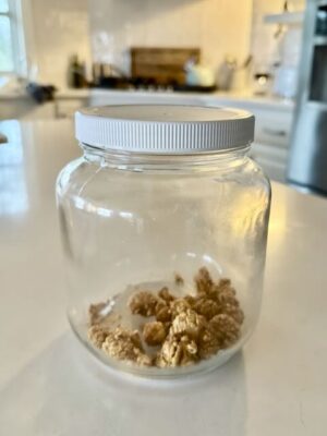 Nearly empty glass jar with just a few pieces of snickerdoodle caramel corn left, sitting on a bright kitchen counter - showing how quickly this sweet, crunchy snack disappears.