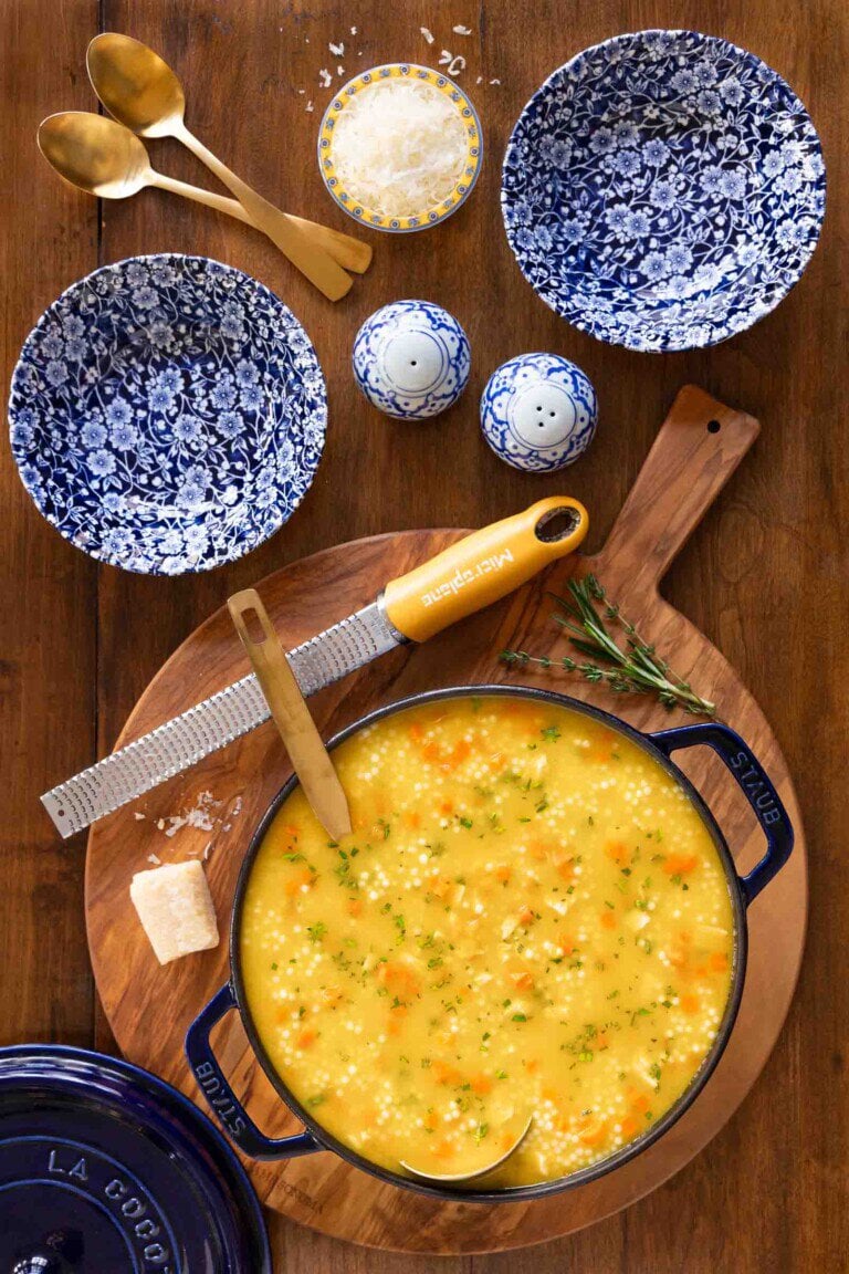 Chicken Pastina Soup in a dutch oven with blue and white bowls on a wooden table.
