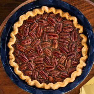 Overhead view of a baked chocolate bourbon pecan pie in a deep-dish blue pie pan, showing the neatly arranged pecan halves and golden, crimped crust.