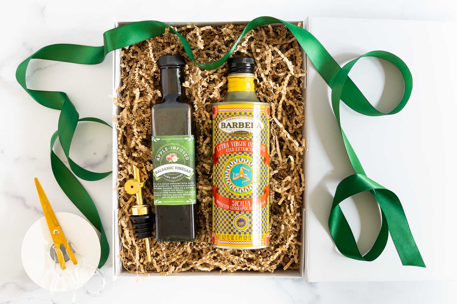Gift box with a bottle of Apple-Infused Balsamic Vinegar and Sicilian olive oil nestled in paper filler with green ribbon and gold pour spout.