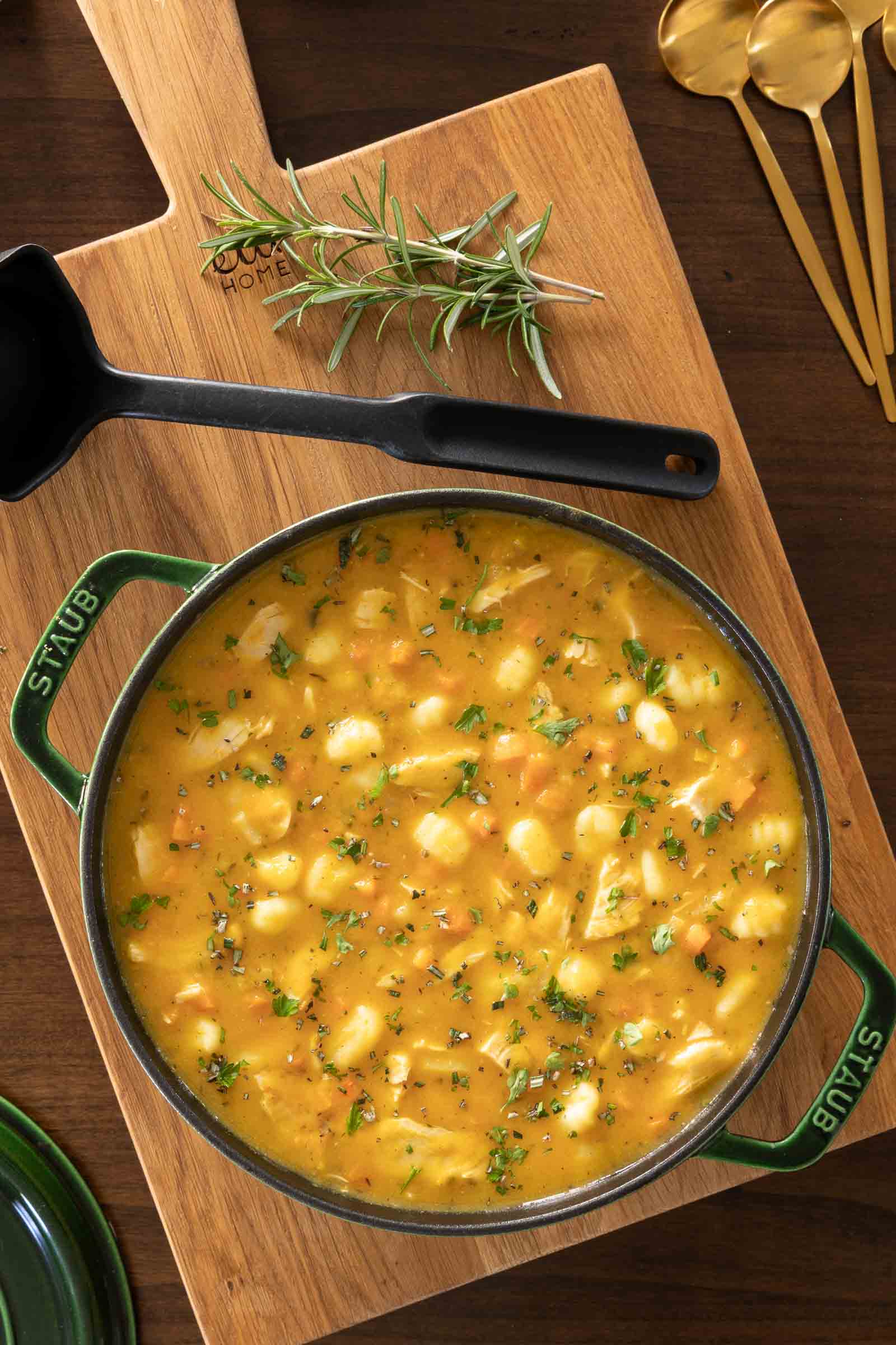 Overhead shot of Leftover Turkey Gnocchi Soup in a pot on a wooden board, garnished with herbs and accompanied by a serving spoon.