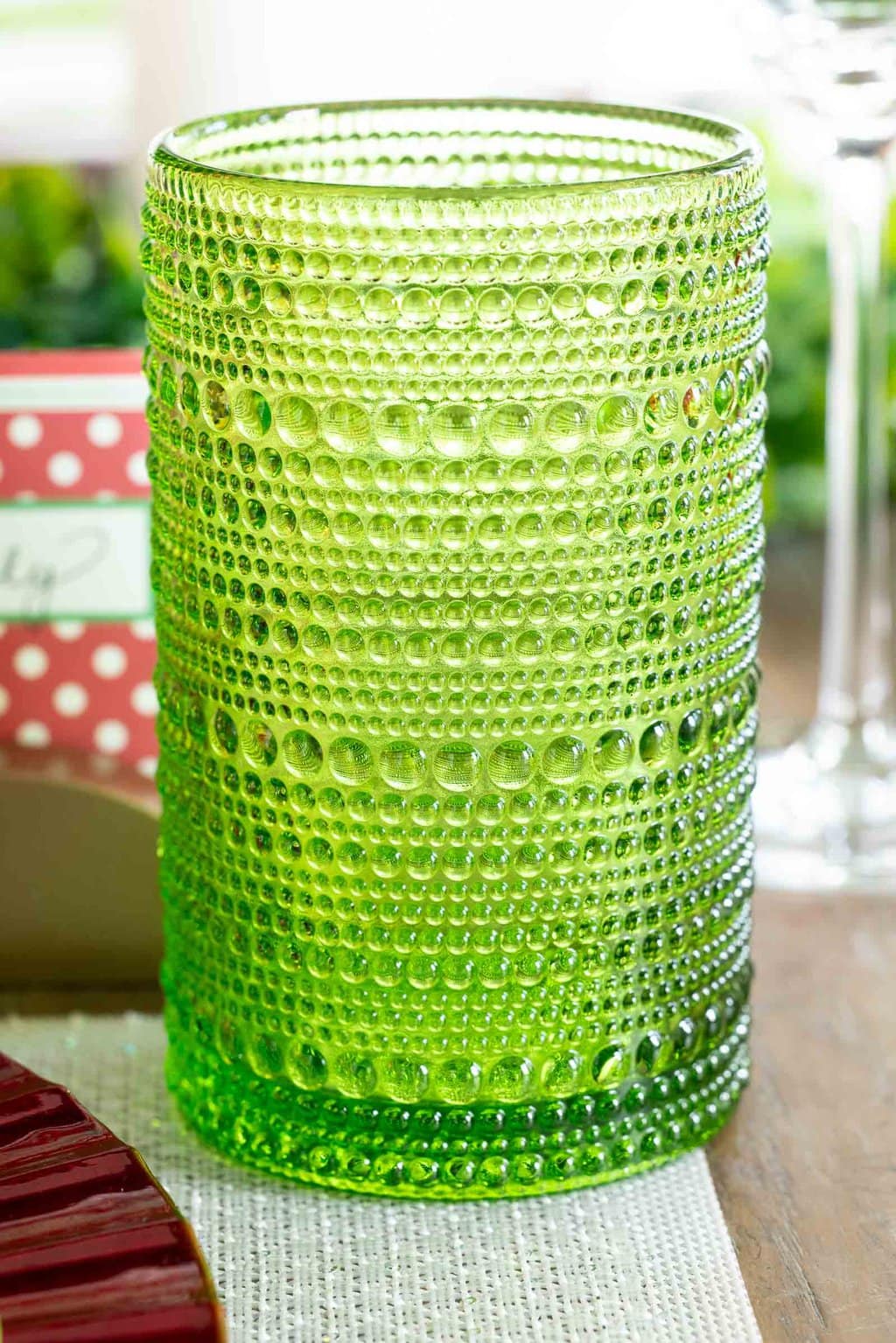 Textured green hobnail drinking glass on a neutral placemat, styled as part of a red and green Christmas tablescape.