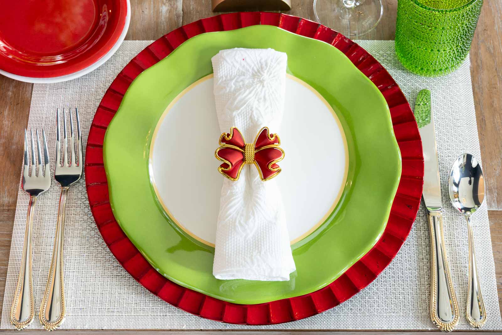 White cloth napkin folded and secured with a red bow napkin ring, placed on layered green and red plates at a Christmas table setting.