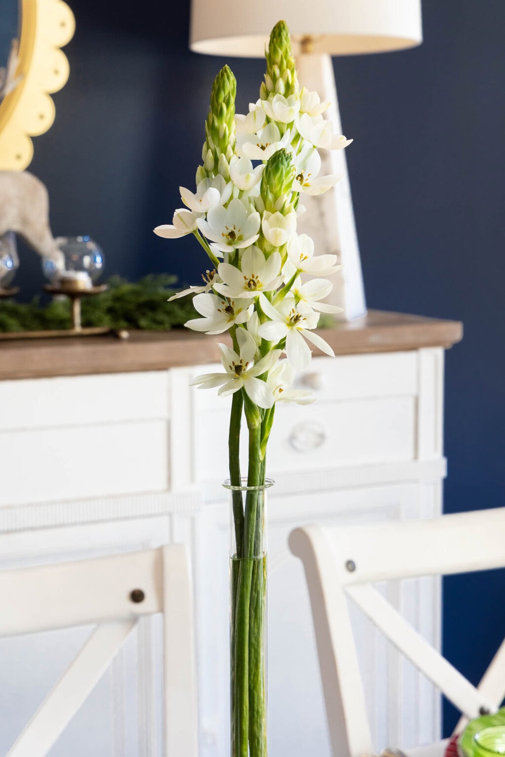 White flowers arranged in a tall clear glass vase, styled as a simple Christmas table centerpiece.
