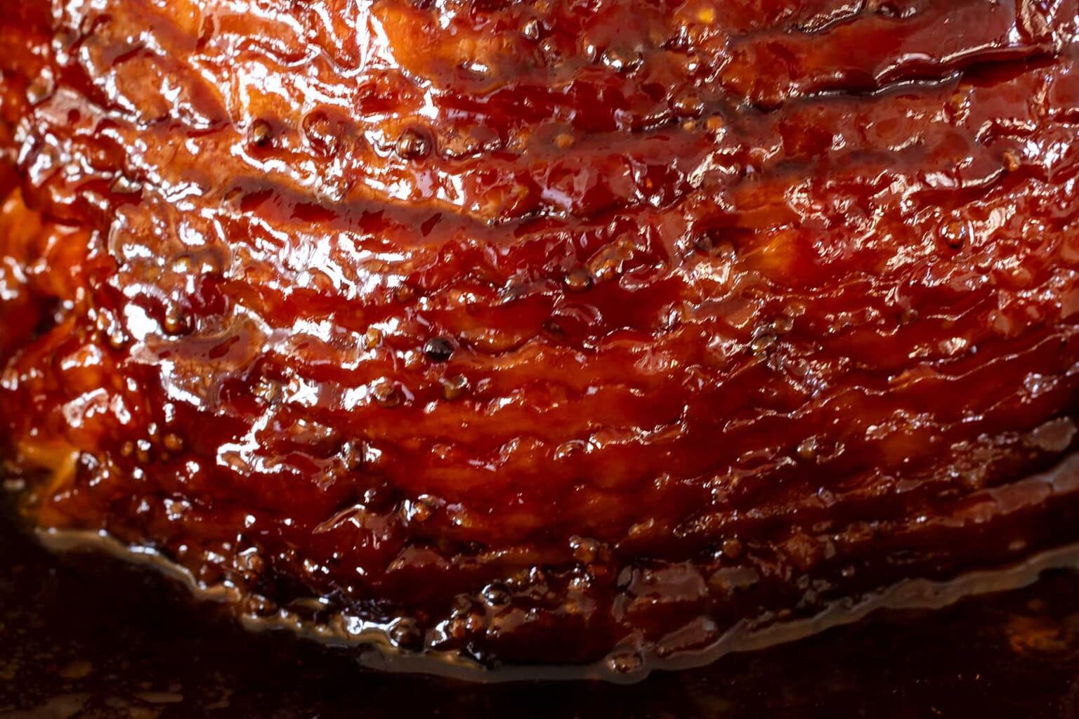 Pepper jelly glazed spiral ham baking in a roasting pan with a glossy caramelized glaze.