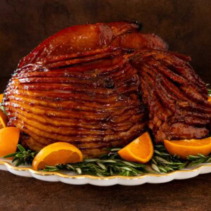 Pepper jelly glazed spiral ham on a serving platter garnished with orange slices and fresh rosemary.
