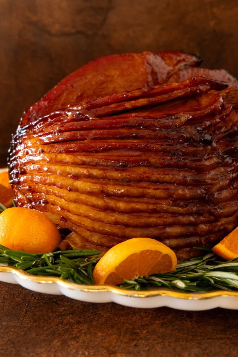 Pepper Jelly Glazed Ham with oranges and fresh herbs on a white platter. 