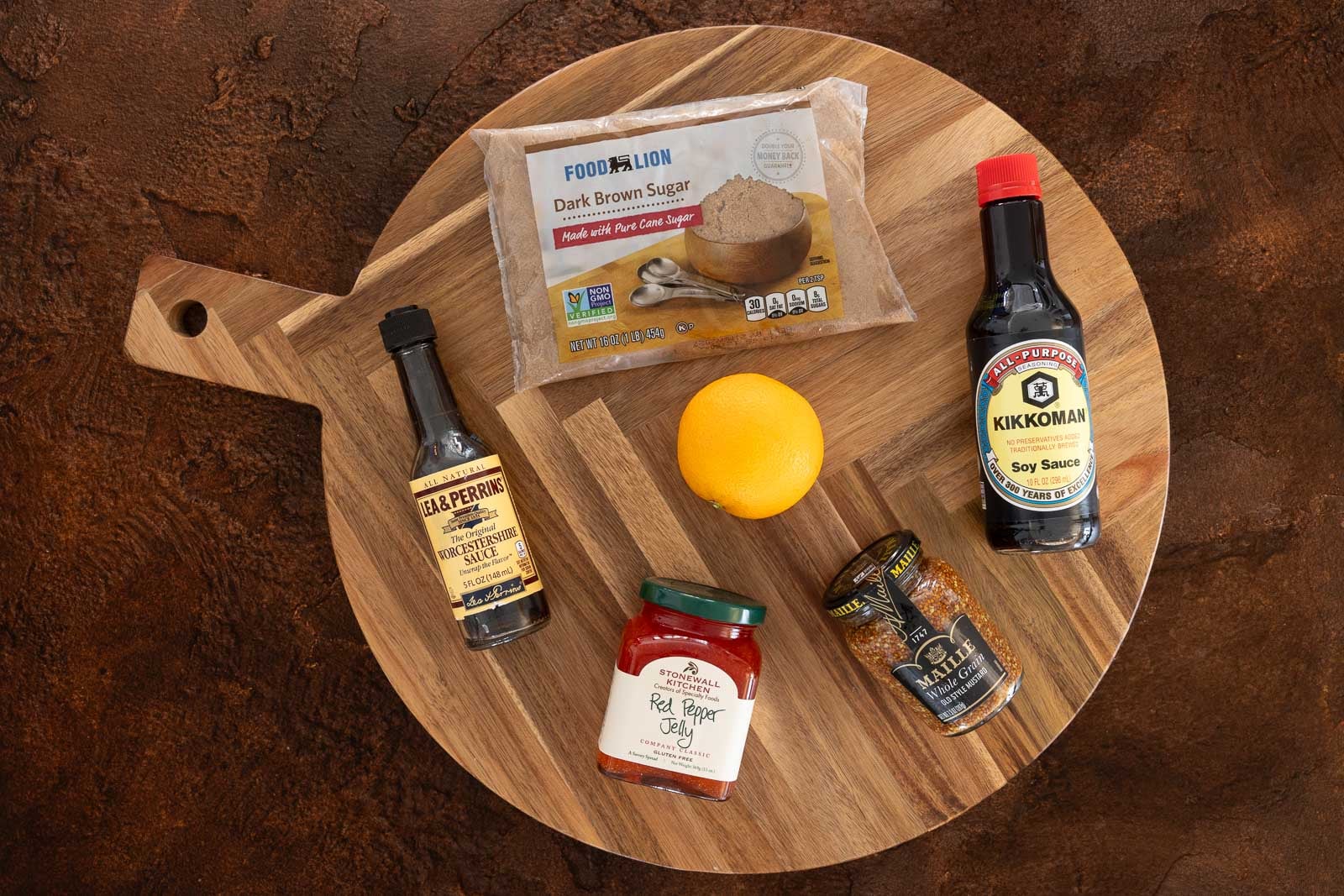 Pepper jelly glazed ham ingredients including pepper jelly, brown sugar, soy sauce, Worcestershire sauce, Dijon mustard, and an orange arranged on a wooden board.