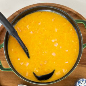 Red lentil and ham soup in a green Dutch oven, partially pureed with visible pieces of ham and vegetables.