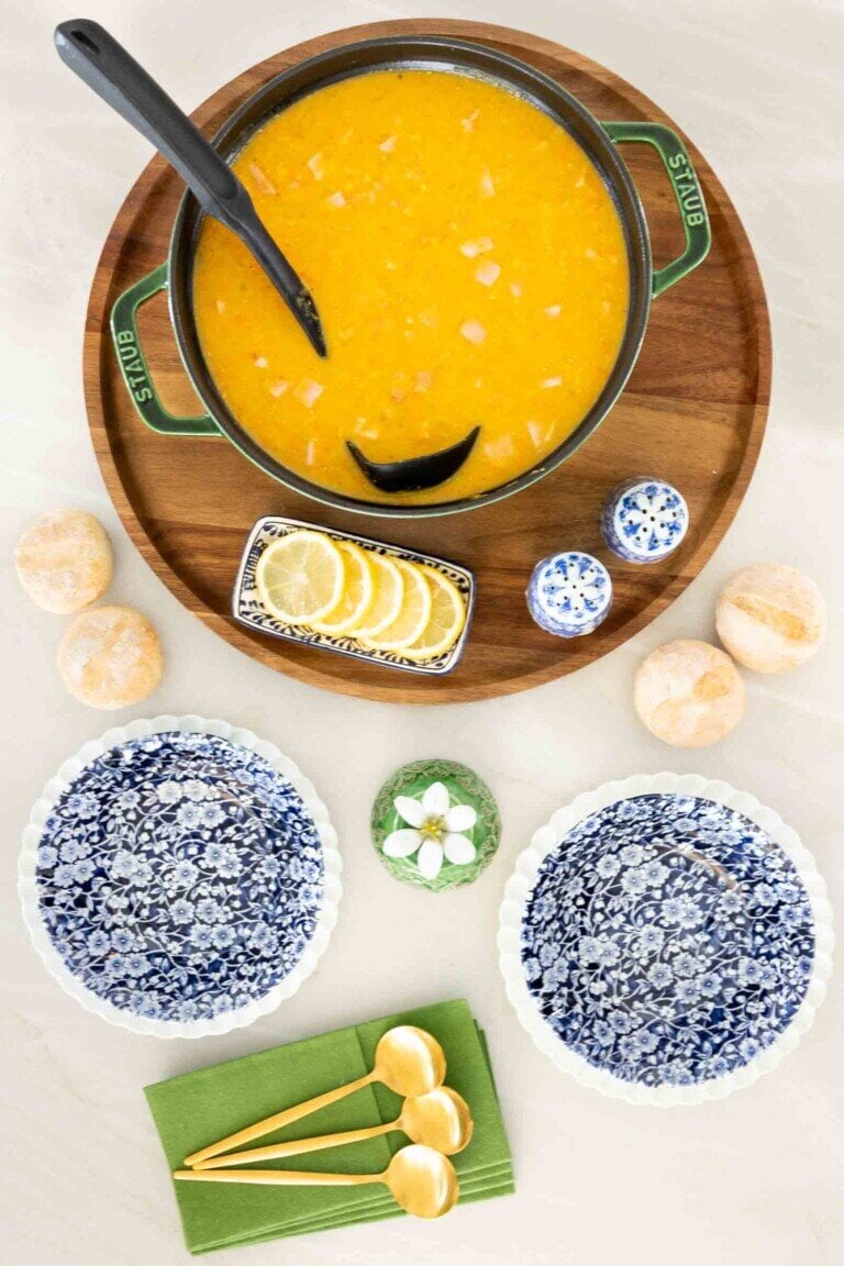 Red Lentil and Ham Soup in a dutch oven on a wooden tray with blue and white bowls, forks and napkins.