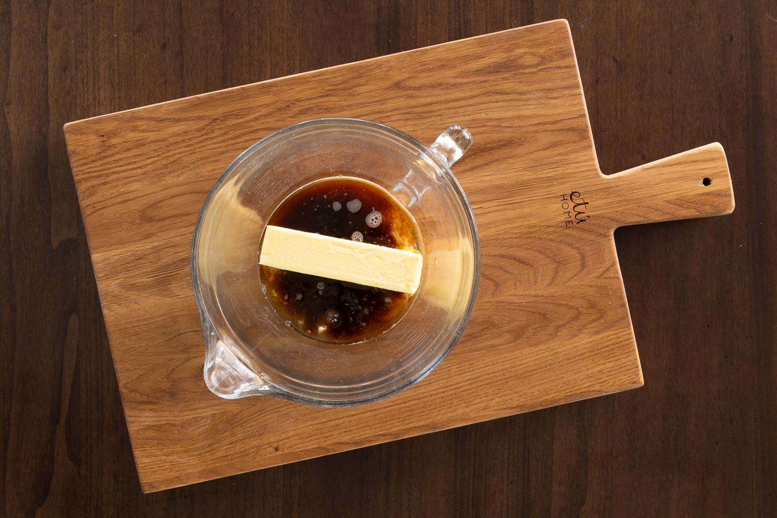 Overhead image of a glass bowl with butter and brown sugar mixture on a wooden board, ready to make microwave English toffee.