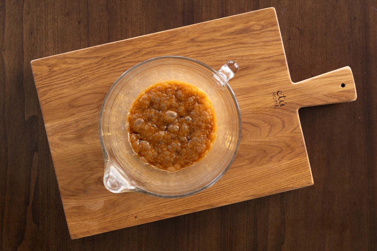 Overhead image of hot, bubbling toffee mixture in a glass bowl on a wooden cutting board.