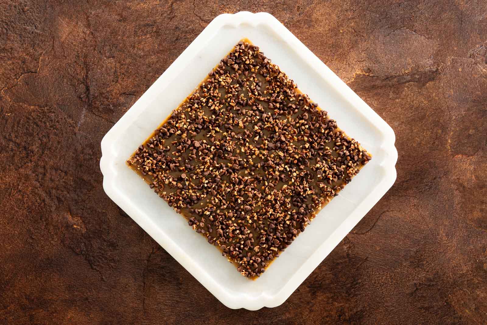 Overhead shot of a full uncut sheet of English toffee topped with chocolate chips and chopped pecans on parchment paper.