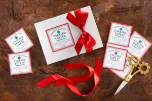 White gift box with a red ribbon surrounded by printable English toffee labels and scissors on a brown surfac