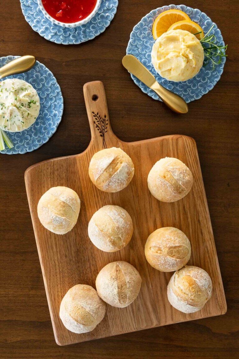 Crusty dinner rolls on a wooden board with compound butters.