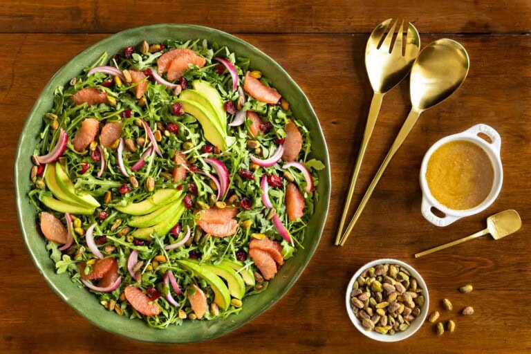 Green salad with arugula, grapefruit segments, sliced avocado, red onion, dried cranberries, and pistachios, served on a green platter with citrus vinaigrette on the side