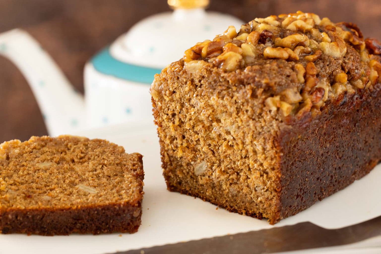 Sliced maple-glazed banana walnut bran muffin loaf showing a moist interior crumb, topped with chopped walnuts and set on a white serving board.