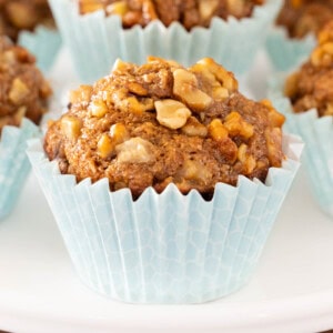 Close-up of a maple-glazed banana walnut bran muffin with a high domed top, baked in a pale blue liner and topped with chopped walnuts.