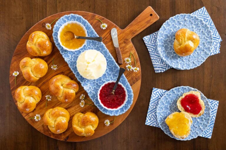 No-knead olive oil challah rolls arranged on a wooden board with butter and jam, photographed from overhead.